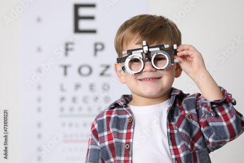 Foto Little boy with trial frame against vision test chart