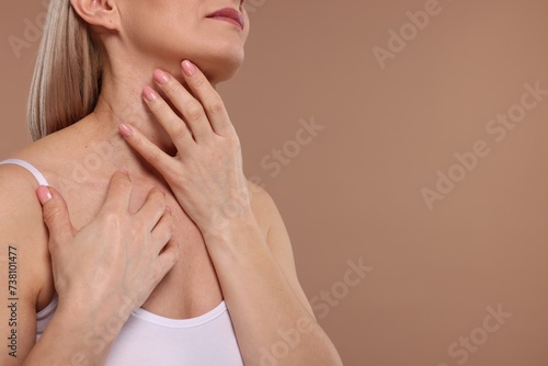 Woman touching her neck on beige background  closeup. Space for text