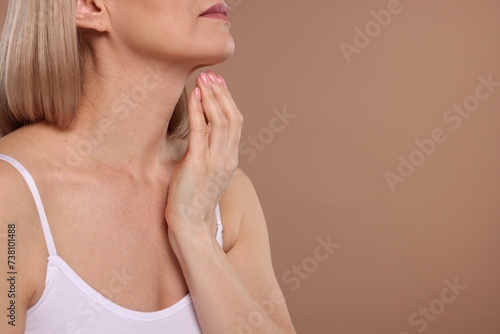 Woman touching her neck on beige background, closeup. Space for text