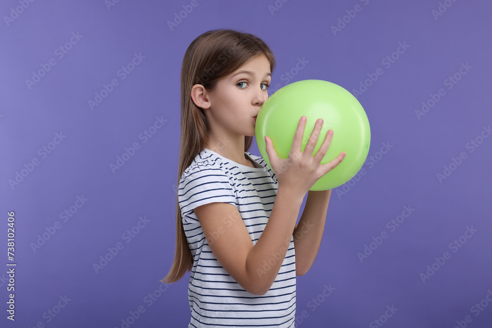 Girl inflating light green balloon on violet background Girl inflating light green balloon on violet background
