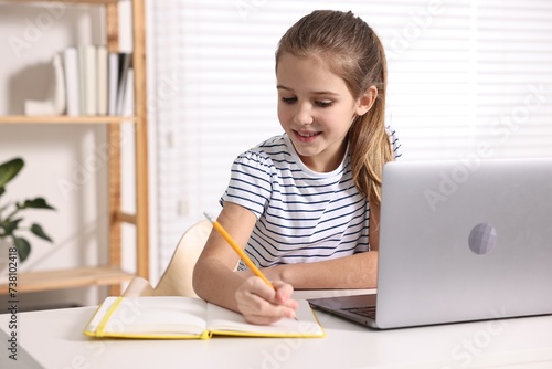 E-learning. Cute girl taking notes during online lesson at table indoors