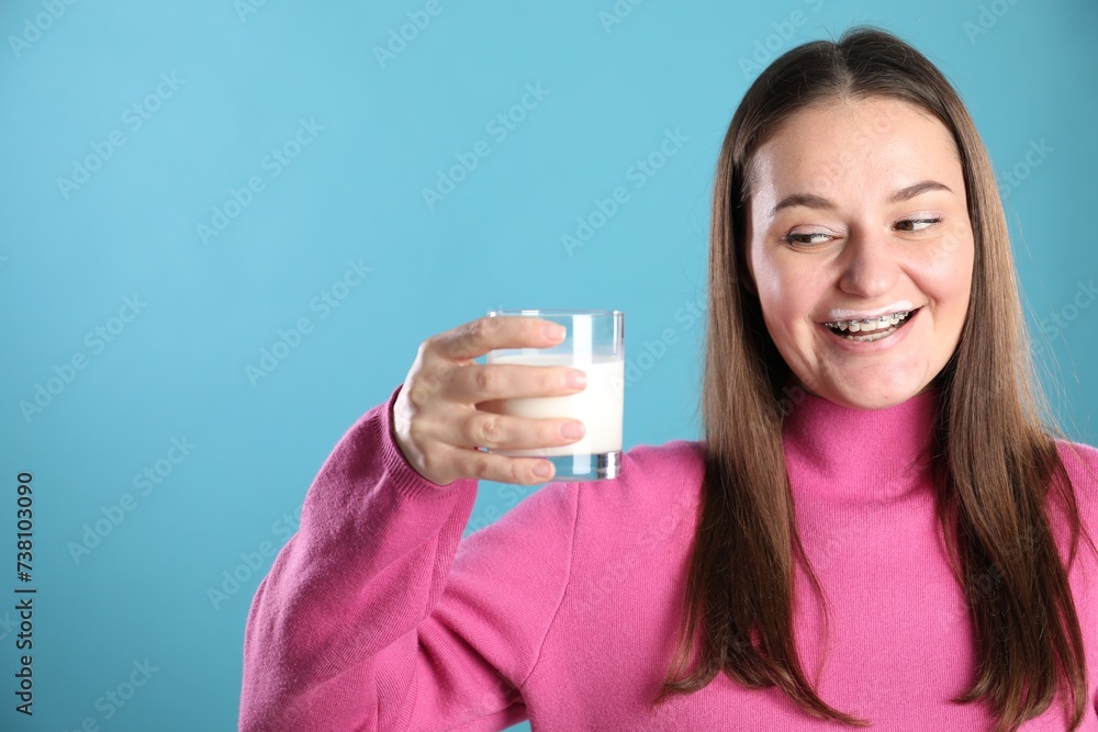Happy woman with milk mustache holding glass of drink on light blue background. Space for text Happy woman with milk mustache holding glass of drink on light blue background. Space for text