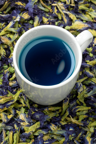 Cup with blue Butterfly pea flower tea and dried butterfly pea tea flowers around it close up