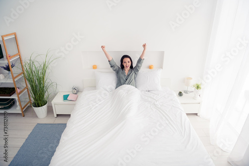 Photo portrait of lovely young lady lying bed raise fists celebrate wear trendy gray sleepwear isolated on white bedroom indoor interior photo