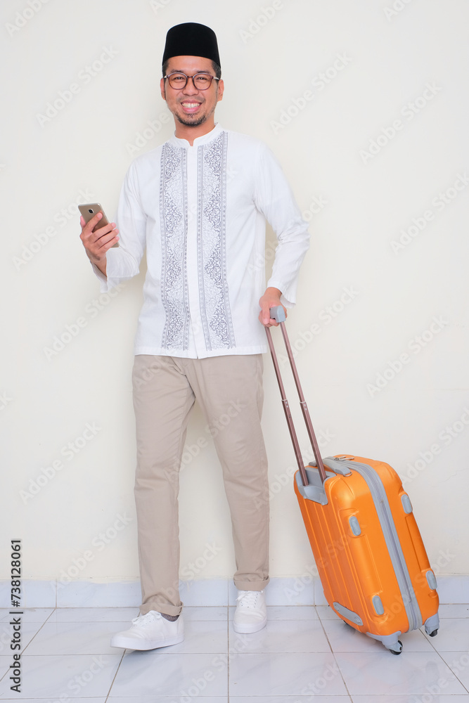 Full body portrait of Moslem man walking with suitcase and holding cellphone Full body portrait of Moslem man walking with suitcase and holding cellphone