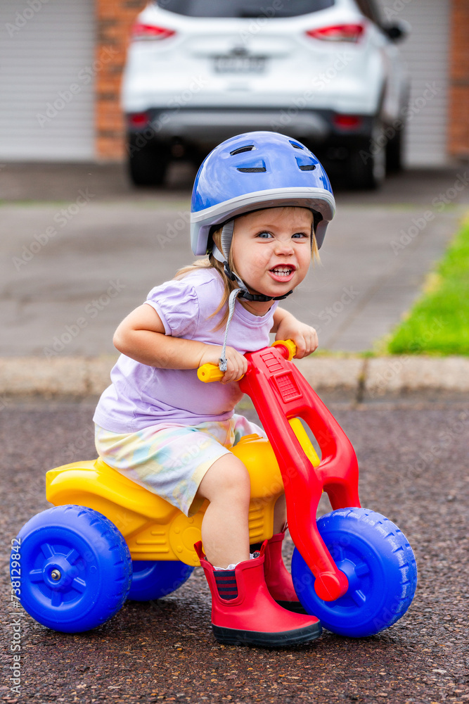 Toddler with cheeky grin riding tricycle on quiet road Toddler with cheeky grin riding tricycle on quiet road
