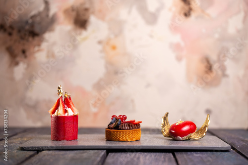 Three fancy desserts with berries on a gray slate board against a mottled pink background