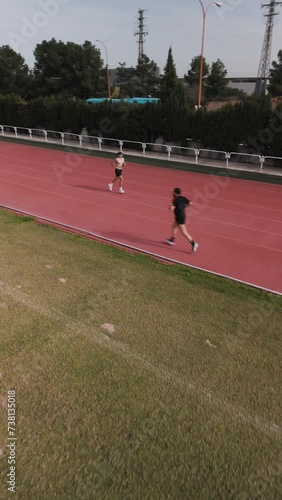 Runner on athletics track running along the central rail. Drone aerial view, vertical video. Sport and healthy life concept