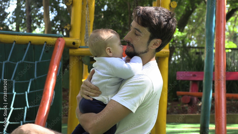 Fototapeta premium Father holding baby son outside at playground park embracing and loving