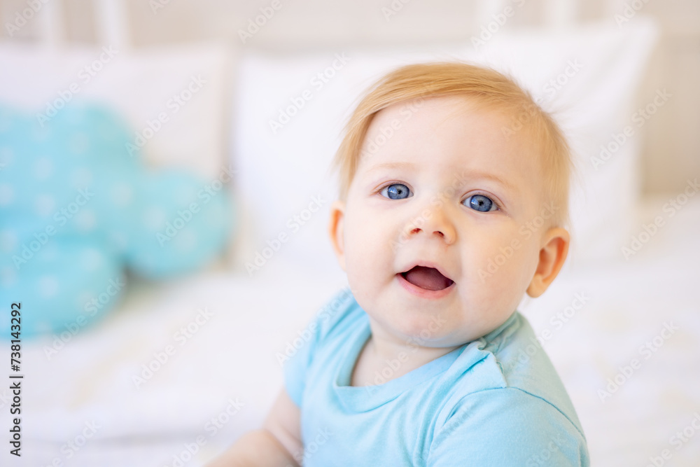 close-up portrait of a small blonde baby, smiling baby with blue eyes at home on the bed close-up portrait of a small blonde baby, smiling baby with blue eyes at home on the bed