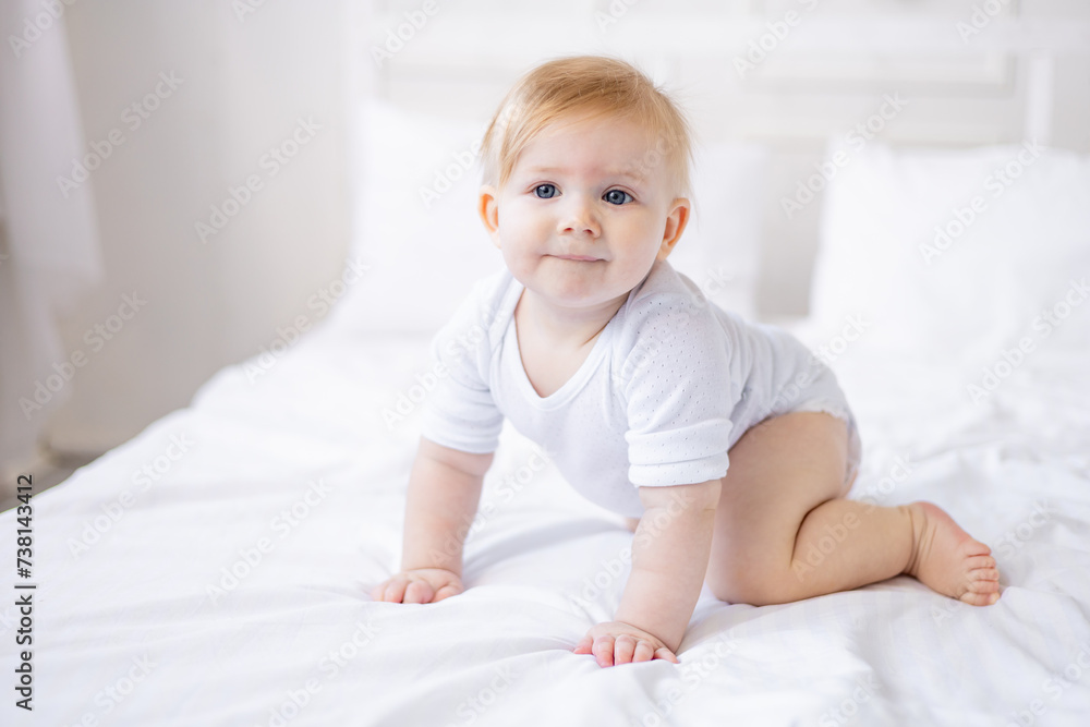 cute smiling baby boy learns to crawl on a white bed at home, little blonde baby woke up in the morning, happy childhood and family cute smiling baby boy learns to crawl on a white bed at home, little blonde baby woke up in the morning, happy childhood and family