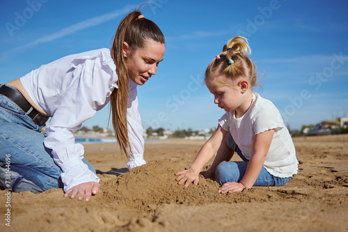 Close up portrait of happy of mother and daughter building castle in sand at beach