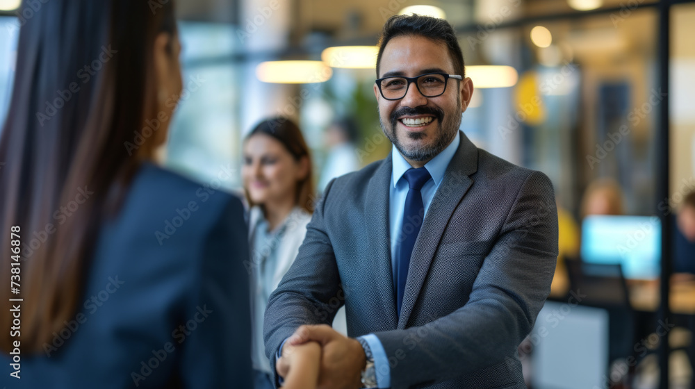 A bearded man in a suit with glasses is smiling and shaking hands with a colleague in a modern office environment. A bearded man in a suit with glasses is smiling and shaking hands with a colleague in a modern office environment.