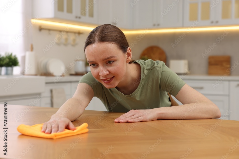 Woman with microfiber cloth cleaning wooden table in kitchen Woman with microfiber cloth cleaning wooden table in kitchen