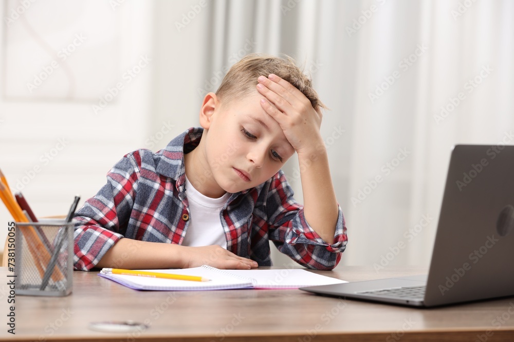 Little boy suffering from headache at wooden desk indoors Little boy suffering from headache at wooden desk indoors