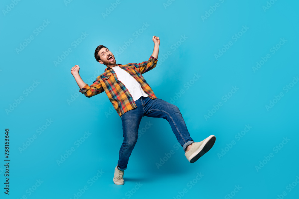 Full size photo of handsome young male dance raise fists cheerful dressed stylish checkered outfit isolated on blue color background Full size photo of handsome young male dance raise fists cheerful dressed stylish checkered outfit isolated on blue color background