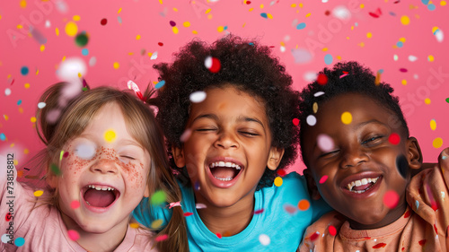 Portrait of three girls friends, face protraits of children of different nationalities in different cloth and hairstyles posing and laughing together at a holiday party with confetti on pink bg photo