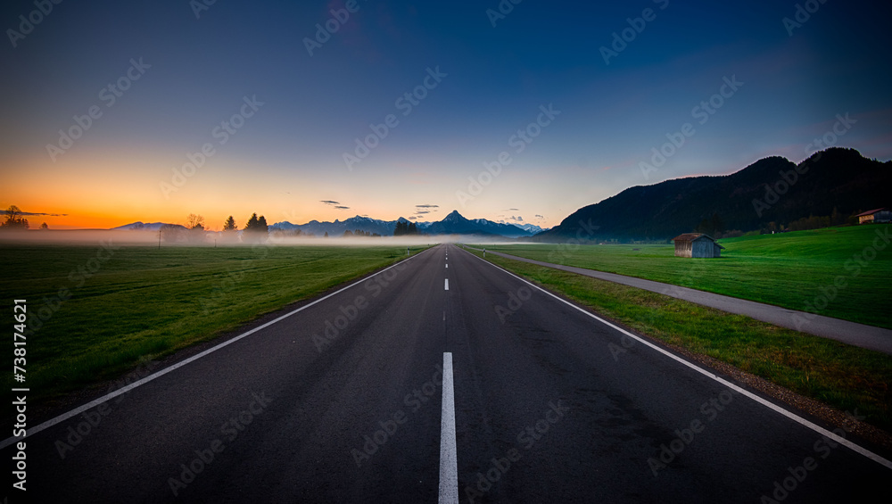 A Scenic Road With a Field and Mountains in the Background A Scenic Road With a Field and Mountains in the Background