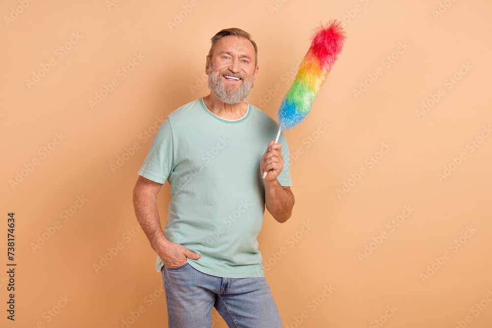Portrait of cheerful aged ma toothy smile hand hold duster empty space isolated on beige color background Portrait of cheerful aged ma toothy smile hand hold duster empty space isolated on beige color background