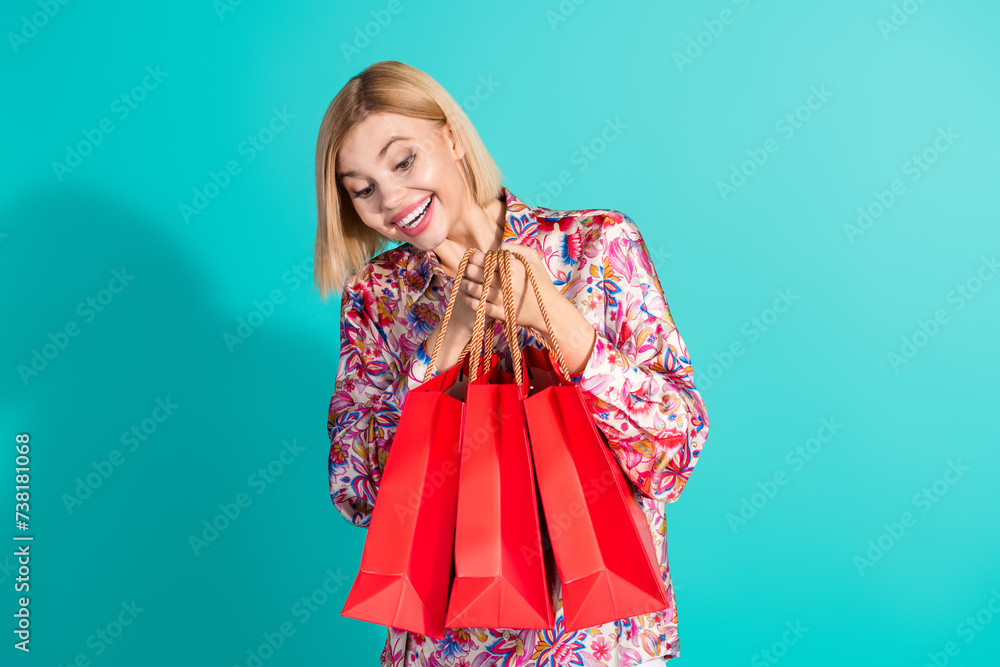 Photo portrait of nice young lady look interested shopping bags dressed stylish pink print garment isolated on aquamarine color background Photo portrait of nice young lady look interested shopping bags dressed stylish pink print garment isolated on aquamarine color background