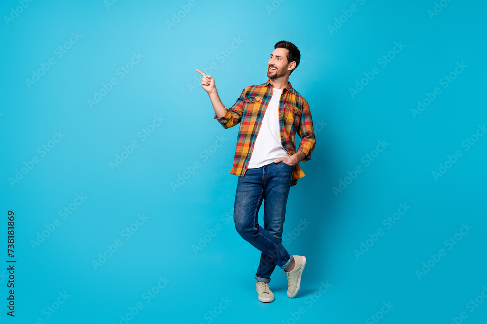 Full length photo of cool guy wear checkered shirt denim pants directing look at discount empty space isolated on blue color background