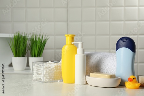 Baby cosmetic products, bath duck, cotton swabs and towel on white table against tiled wall © New Africa