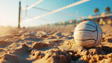 An old worn volleyball on the sand near the volleyball net under a clear blue sky. Outdoor beach volleyball sports competition