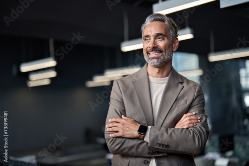 Happy confident mature 45 years old business man investor standing in office looking away. Middle aged rich business owner male ceo executive leader wearing suit at work thinking on future success. photo
