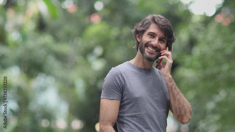 View of a young man with smartphone at daytime in a green park in the city. High quality video. View of a young man with smartphone at daytime in a green park in the city. High quality video.