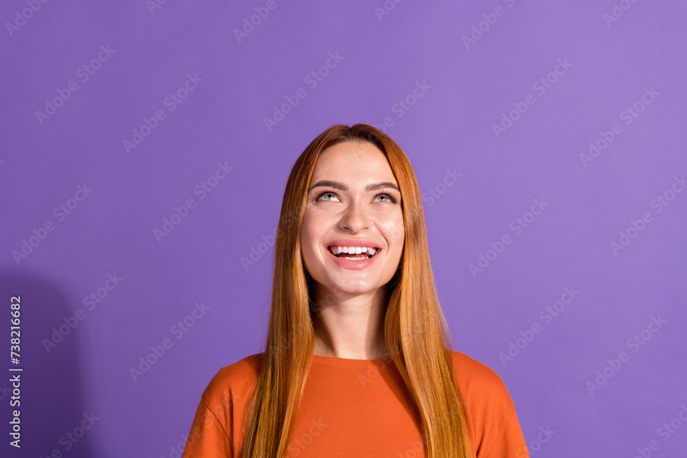 Portrait of young satisfied female model in orange t shirt looking up and enjoying promo video isolated on violet color background Portrait of young satisfied female model in orange t shirt looking up and enjoying promo video isolated on violet color background