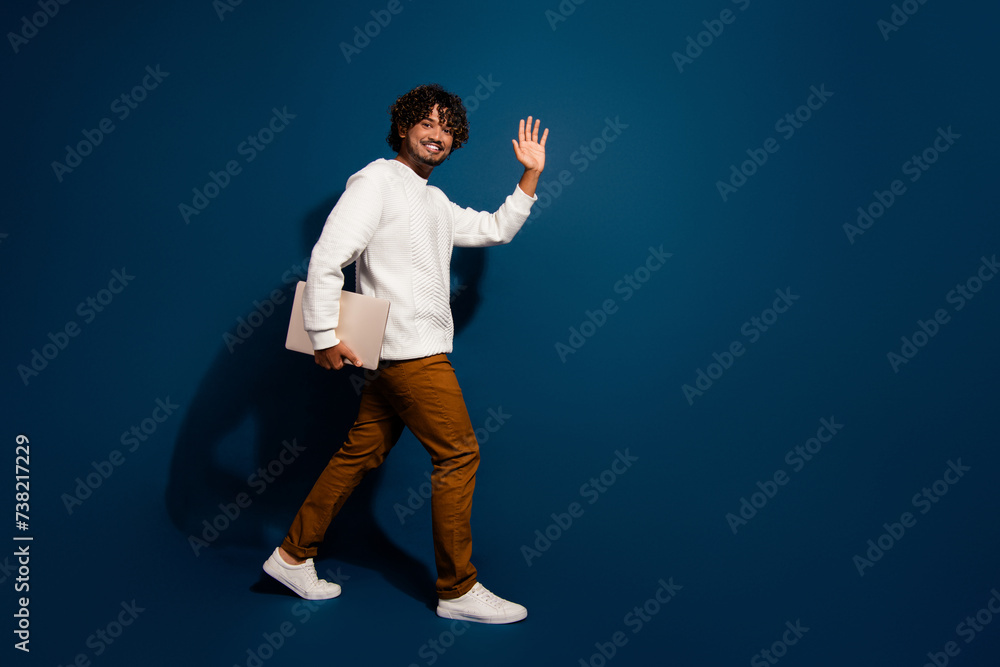 Full length photo of good mood funky guy dressed white pullover holding modern device waving hi empty space isolated dark blue color background Full length photo of good mood funky guy dressed white pullover holding modern device waving hi empty space isolated dark blue color background