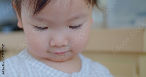 Intimate close-up of a pensive toddler with eyes cast down, in a soft-focus indoor environment.
