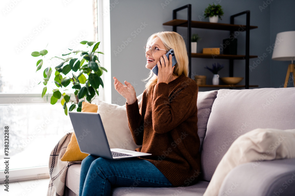 Photo of positive gorgeous retired lady sitting couch talking phone speaking customer client work from home indoors