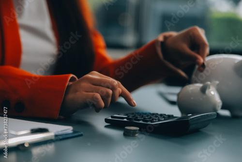 A young girl works at a laptop, writes a business development plan in a notebook, develops a strategy and makes calculations of earned funds. A woman puts her savings in a piggy bank. photo