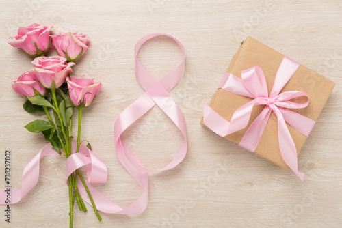 Composition with pink roses, gift box and eight made of ribbon on wooden background, top view. Women's day concept