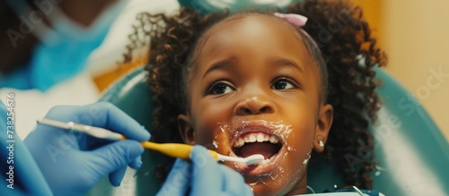 A young girl receives dental education in the dentist s chair while being taught about proper tooth-brushing by a pediatric dentist.