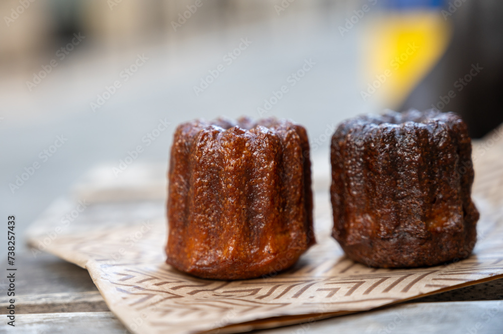 Canele, French pastry flavored with rum and vanilla, soft and tender custard center and dark, caramelized crust specialty of Bordeaux region, France, streets of Bordeaux on background Canele, French pastry flavored with rum and vanilla, soft and tender custard center and dark, caramelized crust specialty of Bordeaux region, France, streets of Bordeaux on background