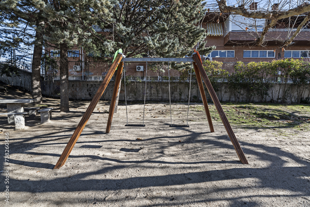 A pair of swings with chains in a recreation area within an urban estate A pair of swings with chains in a recreation area within an urban estate
