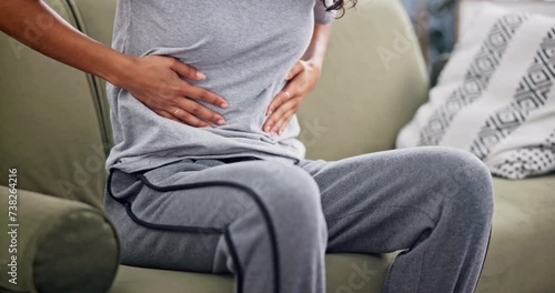 Home, closeup or woman with period pain, sick and digestion problem with menstruation in a living room. Person, apartment or girl in lounge, endometriosis or holding belly for cramps, sick or illness photo