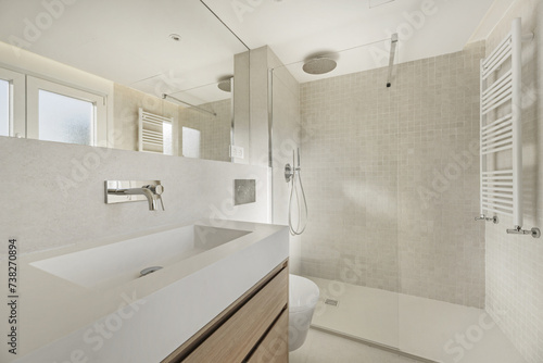 Modern bathroom with elongated white stone imitation sink with wooden cabinet with drawers underneath  suspended toilet  chrome taps  mirror integrated into the wall and towel radiator