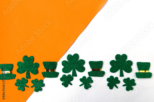 Happy St. Patrick’s Day. Shamrocks and leprechaun hats pattern on white and orange background. Patrick Day symbols on Ireland flag background. Copy space for the text