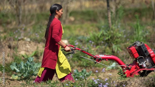 A Nepalese woman uses a mini power tiller to plough soil in her garden, making farming easier and more efficient. This scene highlights the blend of traditional farming with modern technology in rural