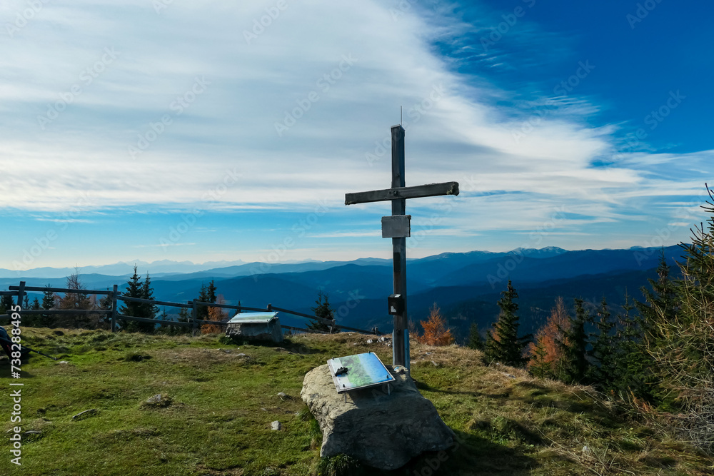 Summit cross on mount Grebenzen with panoramic view of snow capped mountain ridges of Woelzer Tauern seen from Gurktal Alps, Styria, Austria. Calm serene atmosphere in Austrian Alps. Wanderlust Summit cross on mount Grebenzen with panoramic view of snow capped mountain ridges of Woelzer Tauern seen from Gurktal Alps, Styria, Austria. Calm serene atmosphere in Austrian Alps. Wanderlust
