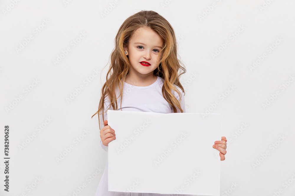 Cute little fashion girl with curly hair and red lips holding a white blank paper with copy space on white background. white sheet mock up Cute little fashion girl with curly hair and red lips holding a white blank paper with copy space on white background. white sheet mock up