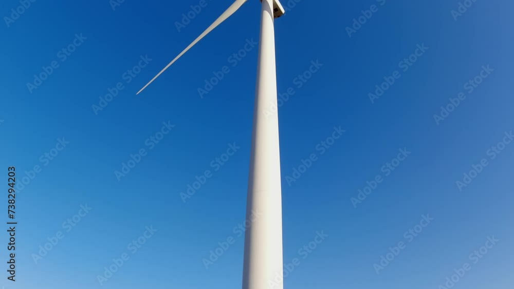 View from below of powerful wind turbine for energy production with clear blue sky. Wind power turbines windmills generating clean sustainable energy. Windmill or wind turbines farm. View from below of powerful wind turbine for energy production with clear blue sky. Wind power turbines windmills generating clean sustainable energy. Windmill or wind turbines farm.