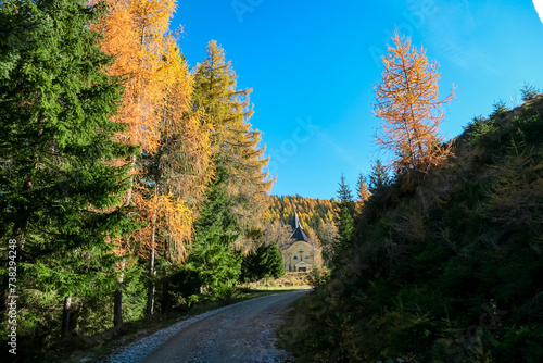 Panoramic hiking trail through idyllic forest in autumn leading to church Schoenanger in Grebenzen  Gurktal Alps  Styria  Austria. Colourful trees in tranquil serene atmosphere in Austrian Alps