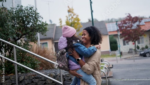 Female nurse, doctor picking up small daughter from kindergarten, preschool, embracing in front school building. Work-life balance of healthcare worker as parent and partner.