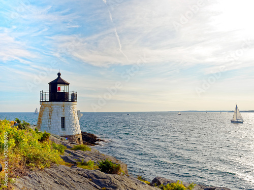 Castle Hill Lighthouse in summer, a beautiful and famous New England light house, Newport, Rhode Island, USA with a sailboat in the distance in Narragansett Bay.