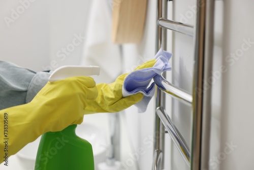 Woman cleaning heated towel rail with sprayer and rag, closeup photo