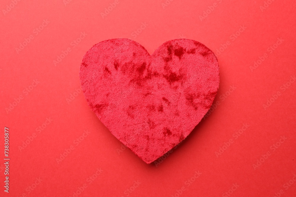 One velvet heart on red background, top view